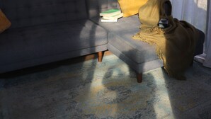 Ein modernes Wohnzimmer mit einem grauen Sofa, einer gelben Decke und Bilderrahmen mit Darstellungen von Gin Tonic und Aperol.