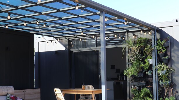 Eine überdachte Terrasse mit Holztable und -stühlen, einer Bank und einer Wand mit Blumentöpfen.