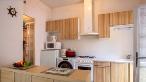 A compact kitchen with wooden cabinets, a microwave, a coffee maker, a washing machine, and a stove. - Rose-May by Interhome (La Bernerie-en Retz)