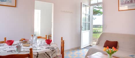 Un coin repas avec une table dressée pour deux personnes, un canapé et une fenêtre donnant sur un paysage verdoyant.