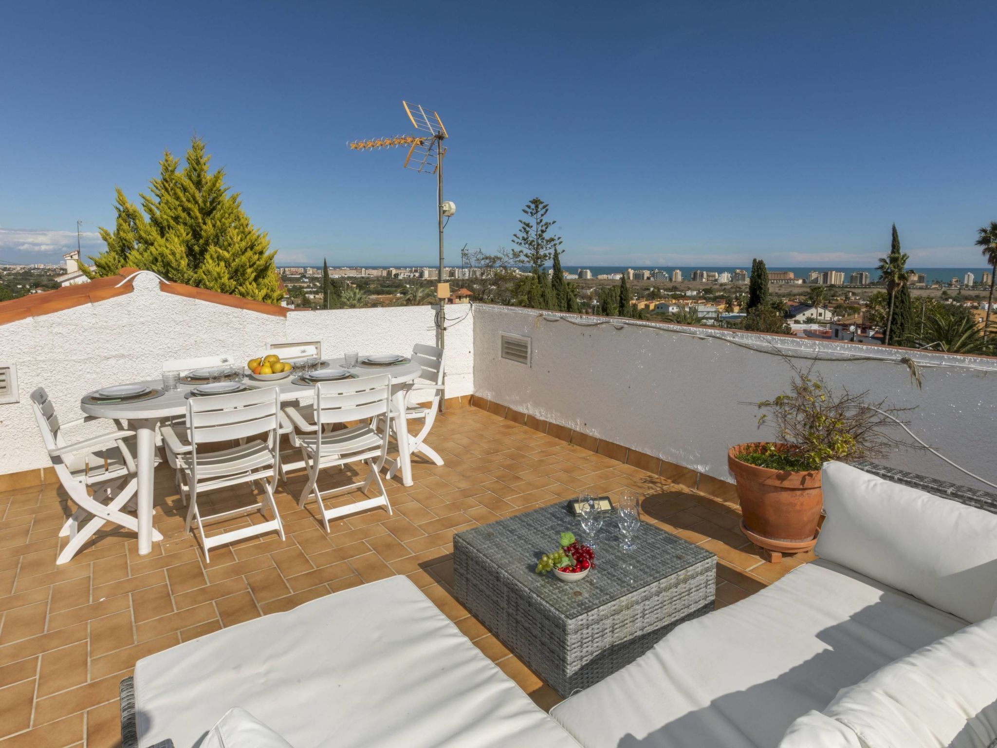 Une terrasse sur le toit avec une table à manger, des chaises, un canapé et un pot de fleurs.