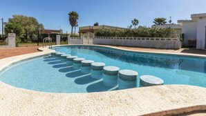 Una piscina amb una zona enrajolada, una porta i una paret blanca amb vegetació.