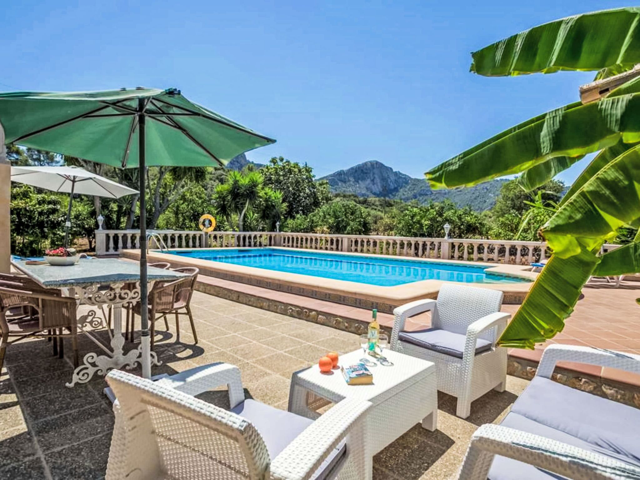 A pool area with a view of mountains, outdoor seating, and a table with chairs.