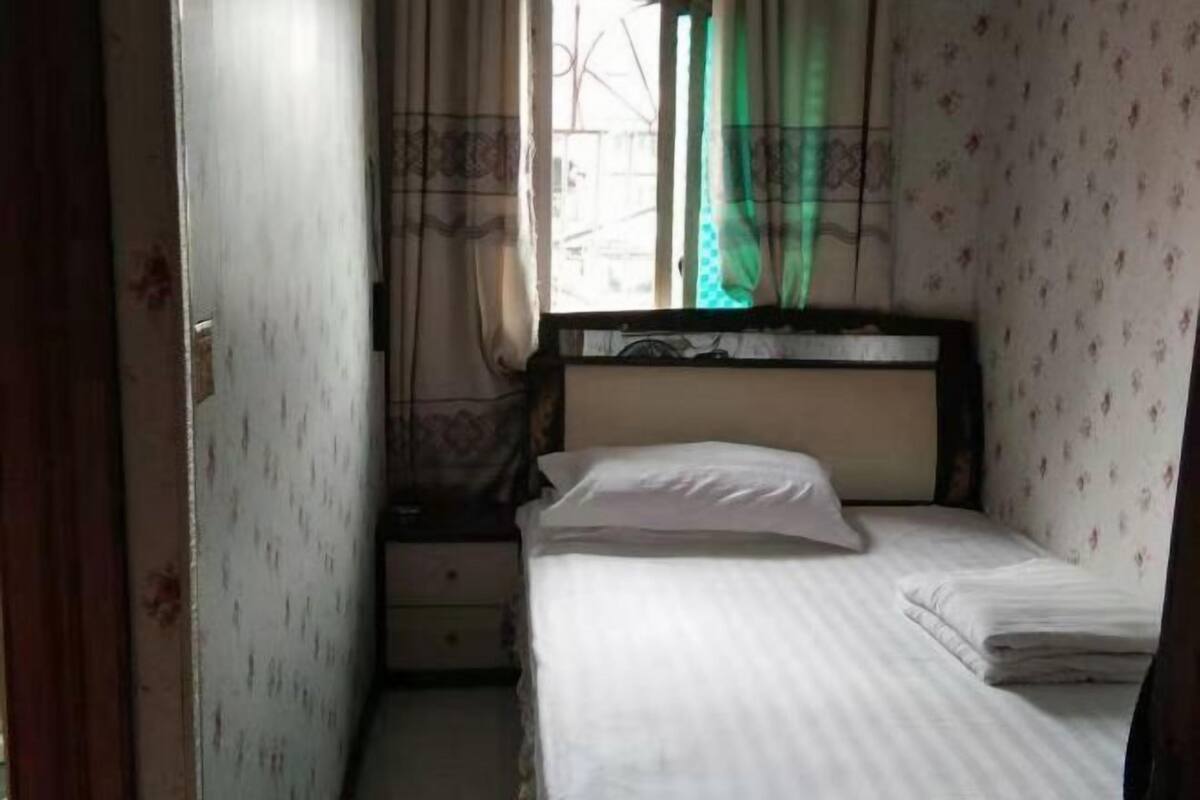 A small, neatly made bed with a wooden headboard in a room with floral wallpaper.