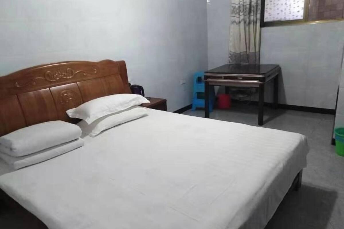 A neatly made bed with a wooden headboard, a small bedside table, and a chair with a table beside it.