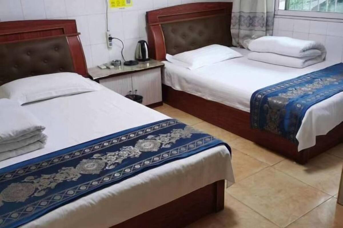 A hotel room with two beds, a nightstand, and a window with curtains.