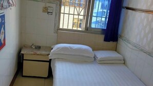 Una habitación pequeña y limpia con una cama individual, una mesita y una ventana con vistas al exterior.