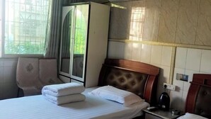 Habitación de hotel con cama, armario, mesita de noche con tetera y ventana con vistas a zonas verdes.