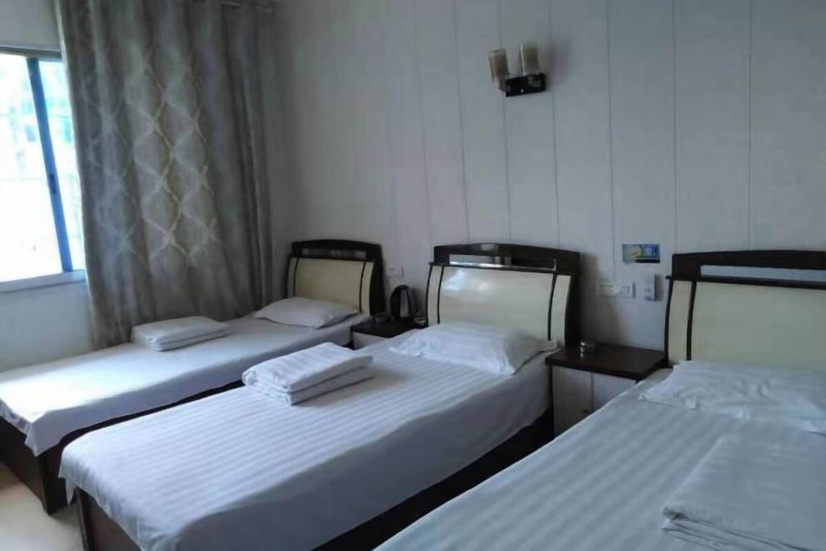 A hotel room with three single beds, a bedside table with a lamp, and a window with curtains.