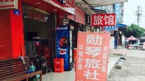 Un hotel con fachada roja y un anuncio de Pepsi. Hay un banco afuera y una gran cartelera con caracteres chinos.