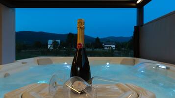 Ein Whirlpool mit einer Champagnerflasche und einem Glas, mit Blick auf Berge und ein Haus.