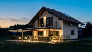 Ein zweistöckiges Haus mit Balkon, überdachter Terrasse und Rasenfläche.