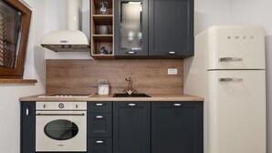 Eine kleine Küche mit einem weißen Kühlschrank, dunklen Schränken, einer Holz Arbeitsplatte, einem eingebauten Backofen und einem Fenster mit Jalousien.