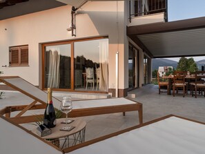 A modern outdoor patio with a table set for two, a bottle of champagne, and a glass.