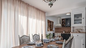 Ein Essbereich mit einem Holztisch, gedeckt für vier Personen, umgeben von Stühlen mit floralem Bezug. Im Hintergrund ist ein weißes Schrank mit Glastüren zu sehen.
