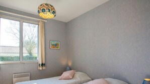 A bedroom with two beds, a window with curtains, a radiator, a lamp, and a picture on the wall. - La Bruyère by Interhome (La Bernerie-en Retz)