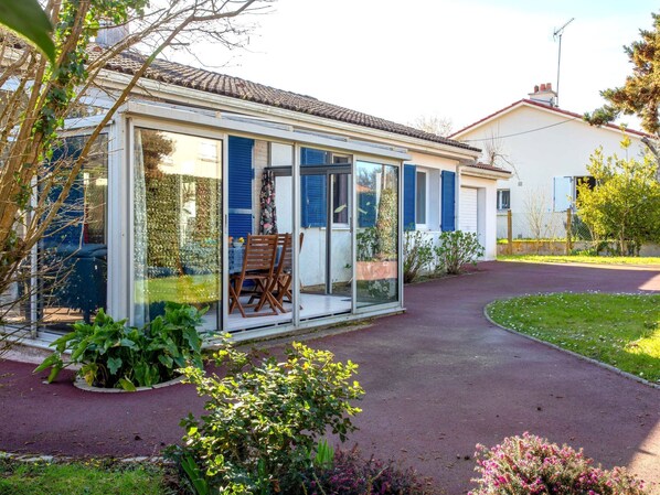 A house with a glass conservatory, a patio with a table and chairs, and a garden with various plants.