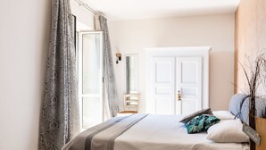 A bedroom with a bed, a bedside table, a chair, a wardrobe, and a window with curtains. - Al Forte by Interhome (Arnasco)