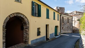 A narrow street with a yellow building featuring an arched entrance and green shutters. - Al Forte by Interhome (Arnasco)