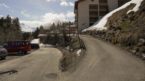 A road leading to a multi-story building with balconies, surrounded by snow-covered hills and trees. - Grand Vue 01-02 by Interhome (Thyon-Les Collons)
