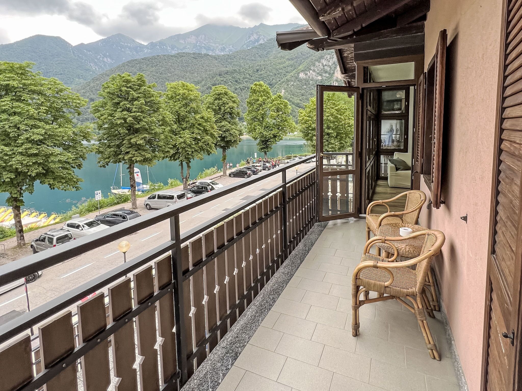 A balcony with wicker chairs overlooking a road with parked cars and a lake.