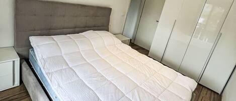 A modern bedroom with a bed, a nightstand, and a wardrobe.