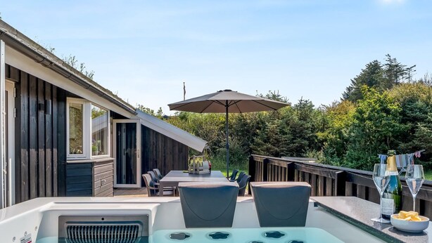 Ein Whirlpool mit Tisch und Stühlen, eine Holzterrasse und ein großer Sonnenschirm.
