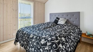 Ein Schlafzimmer mit einem großen Bett, einem grauen gepolsterten Kopfteil und einem Fenster mit Jalousien.
