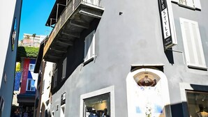 En bygning med en privat terrasse markeret med en gul pil, en butiksvindue med mannequiner, og en klar blå himmel.