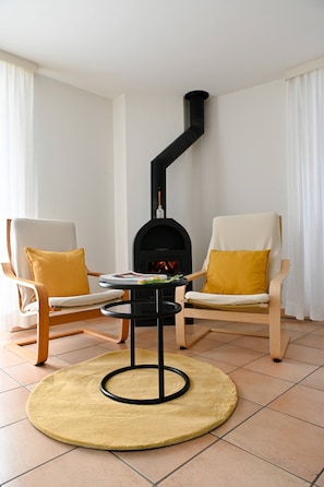 Ein Zimmer mit Kamin, zwei Sesseln mit Kissen, einem runden Tisch und einem Teppich.