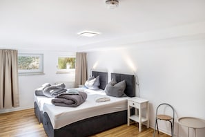 Un dormitorio con cama, mesita de noche, silla y ventana.