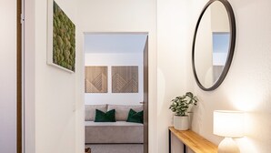 Ein Flur mit einer Holzbank, einem Spiegel, einer Topfpflanze und einem Sofa mit grünen Kissen.