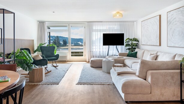 Ein modernes Wohnzimmer mit einer Couch, einem Couchtisch, einem Fernseher und Blick ins Freie.