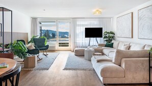 A modern living room with a sofa, a coffee table, a TV, and a view of the outdoors.