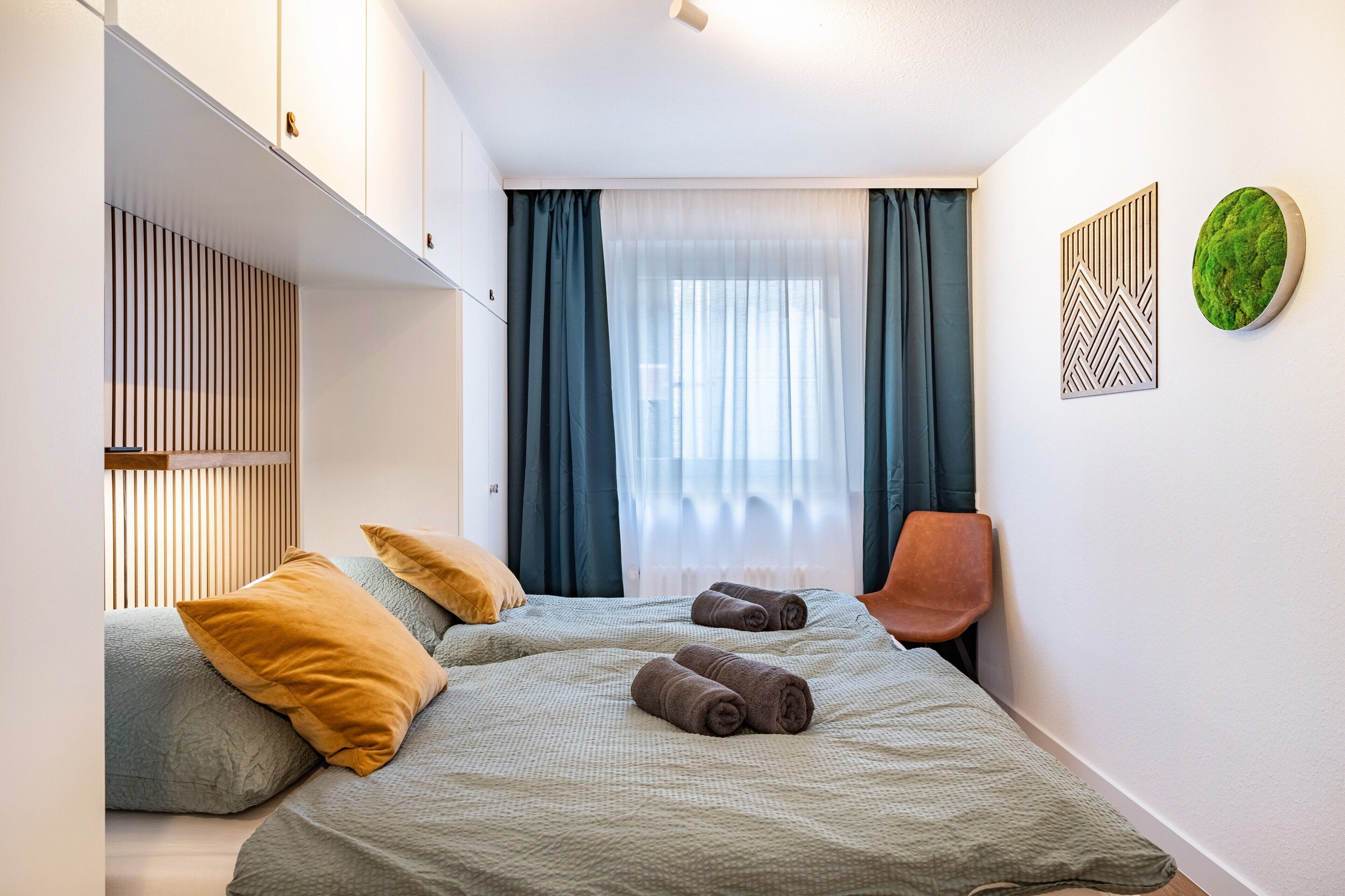 Ein Schlafzimmer mit zwei Betten, einem Sessel, einer Wandleuchte und einer Wanddekoration in Grün.