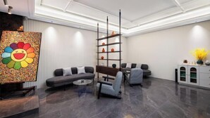 A modern living room with a gray sofa, a patterned armchair, a coffee table, and a tall shelving unit with decorative items. - CEO· Lan Hotel (Yiwu)