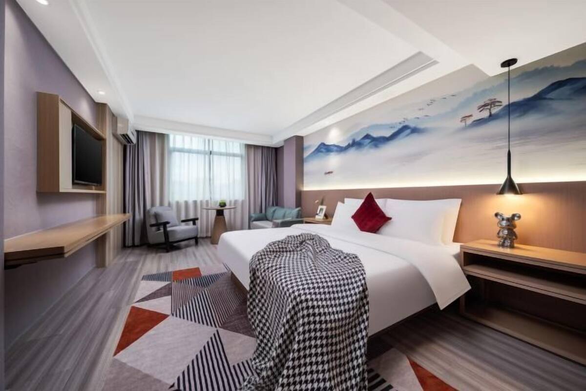 A hotel room with a bed, a desk, a chair, a TV, and a painting on the wall.