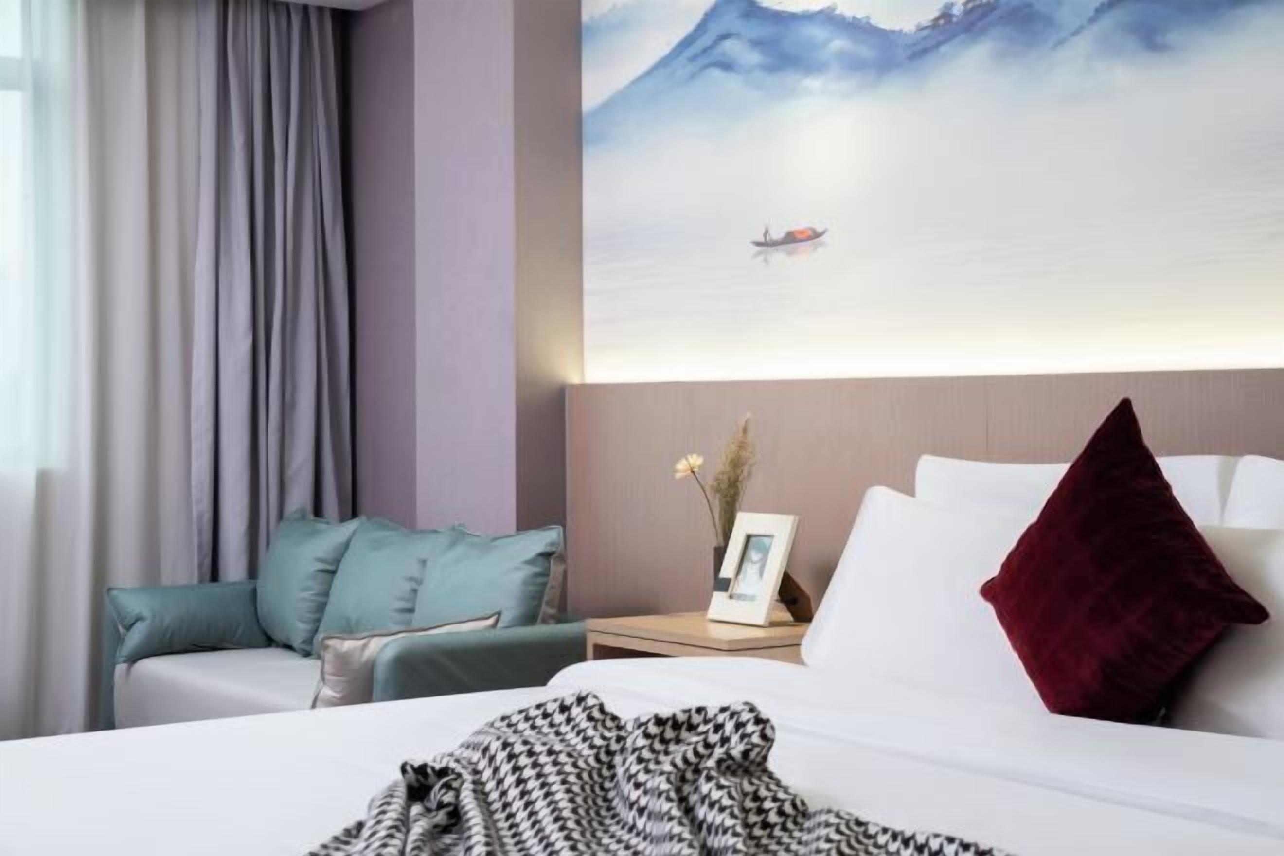 Een hotelkamer met een bed, een nachtkastje met een bloevas, een schilderij van een berglandschap en uitzicht op zee.