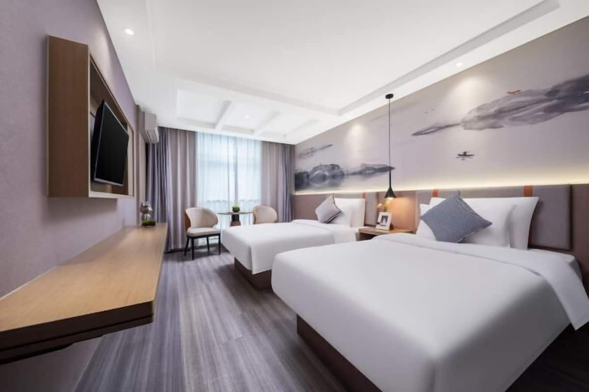 A hotel room with two beds, a TV, a desk, and a large window.
