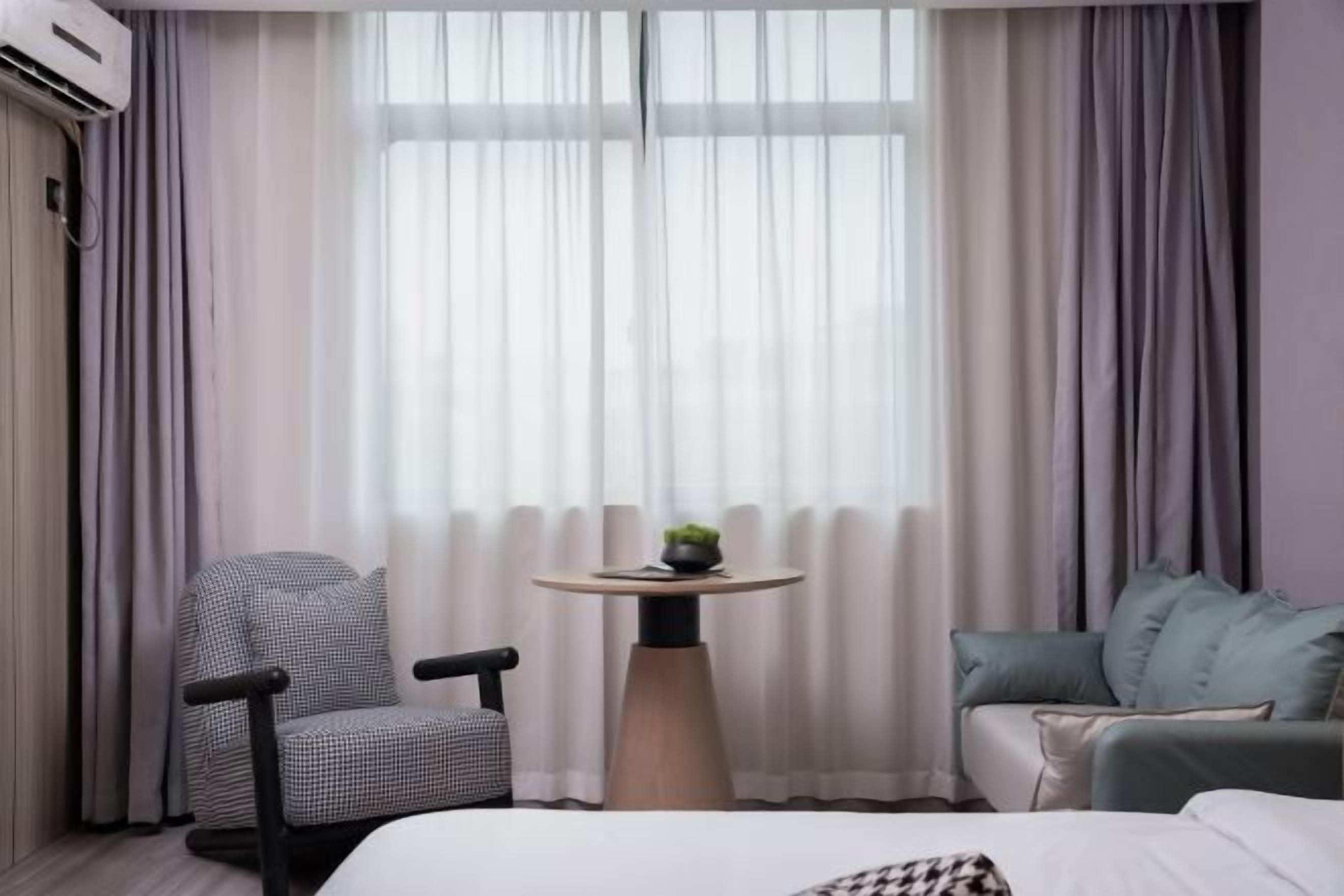 A hotel room with a bed, a round table with a plant, a chair, and a sofa.