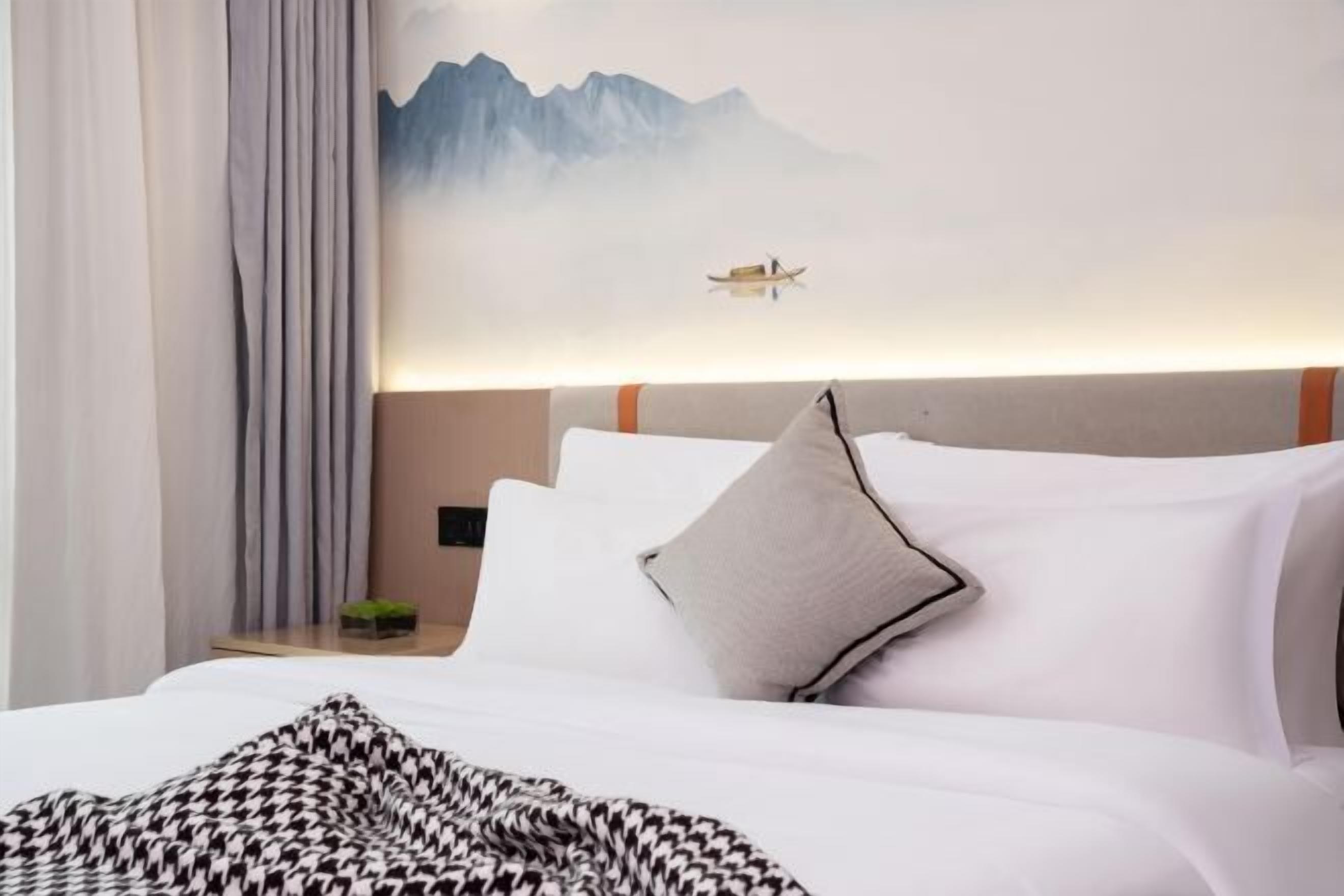 A neatly made bed with white linens, a patterned throw blanket, and a mountain landscape painting above it.