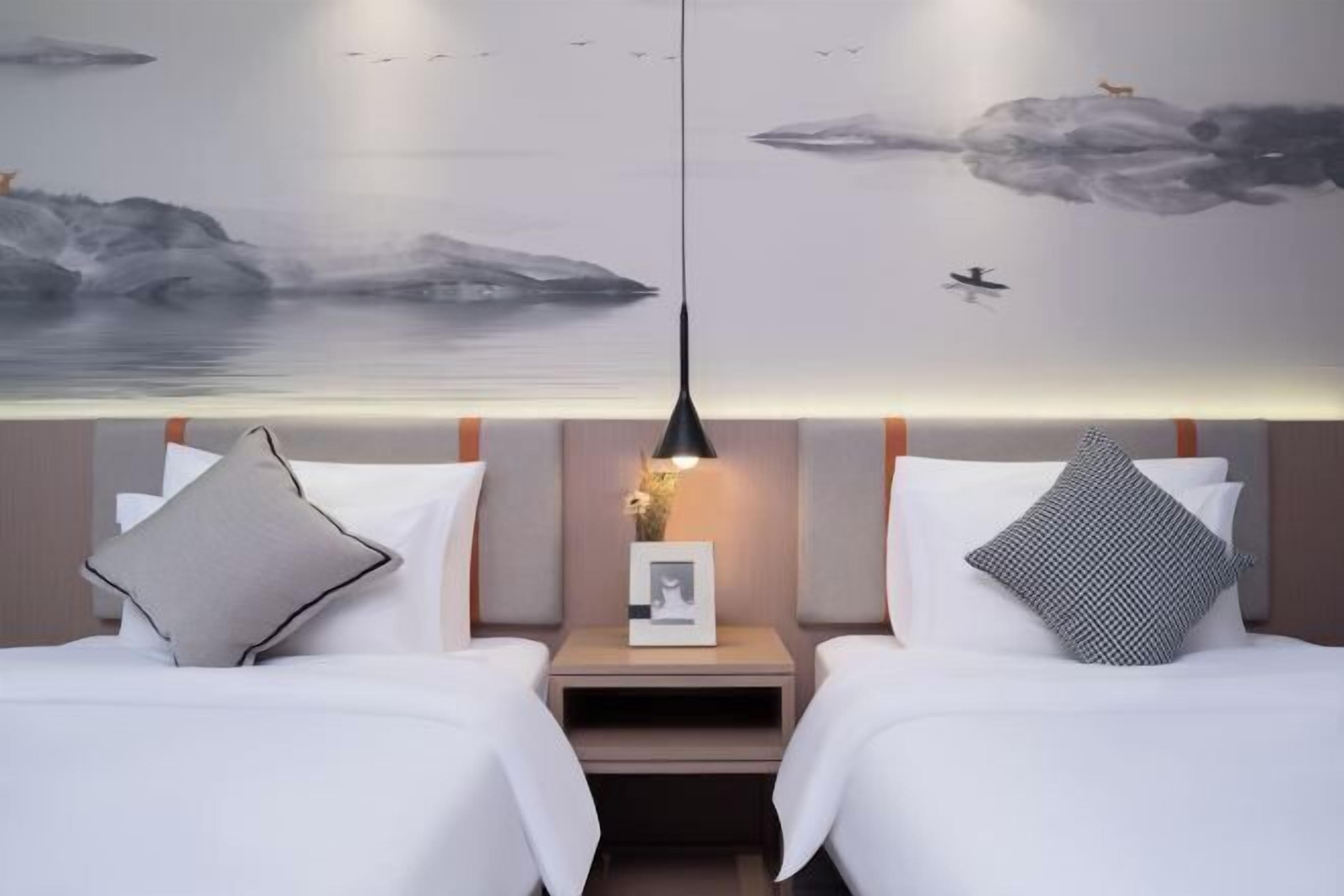 Quarto de hotel com duas camas, uma mesa de cabeceira com luminária e um mural na parede.