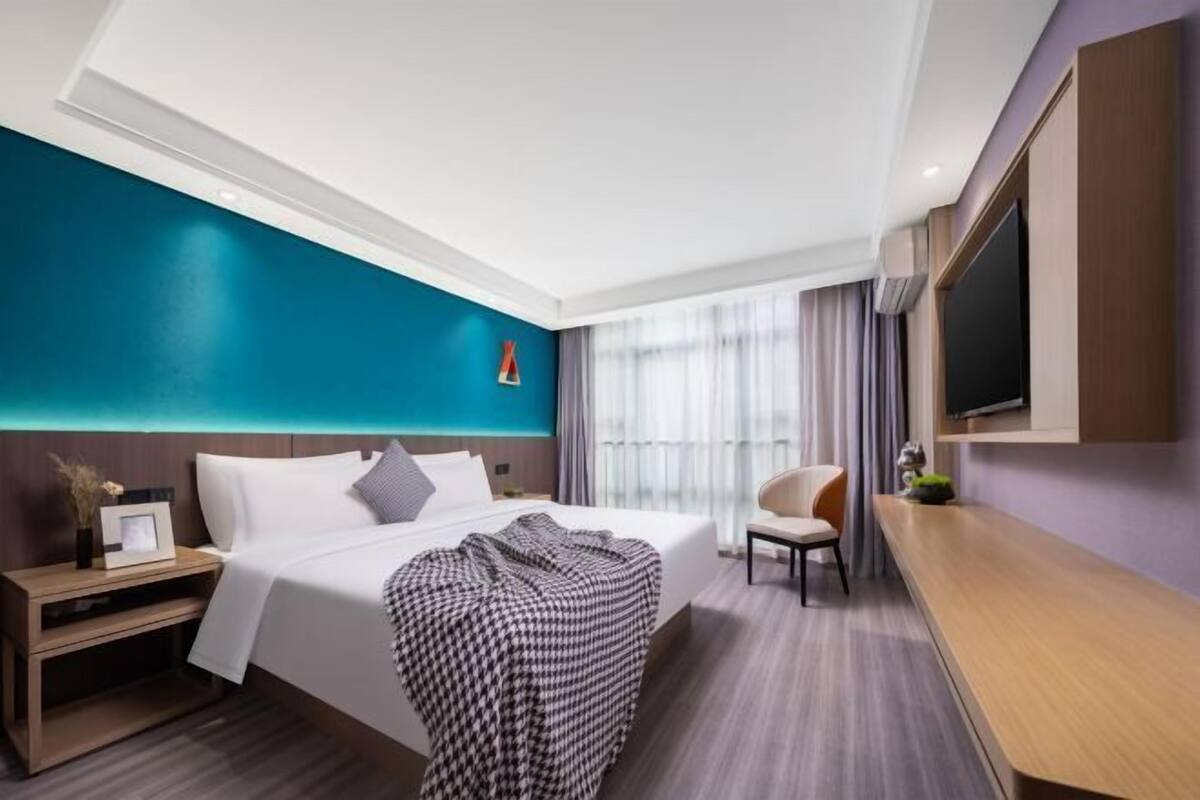 A hotel room with a bed, bedside table, TV, and a view of the outdoors.