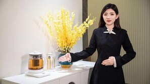 A person standing next to a white table with a vase of yellow flowers, a coffee maker, and a scale. - CEO· Lan Hotel (Yiwu)