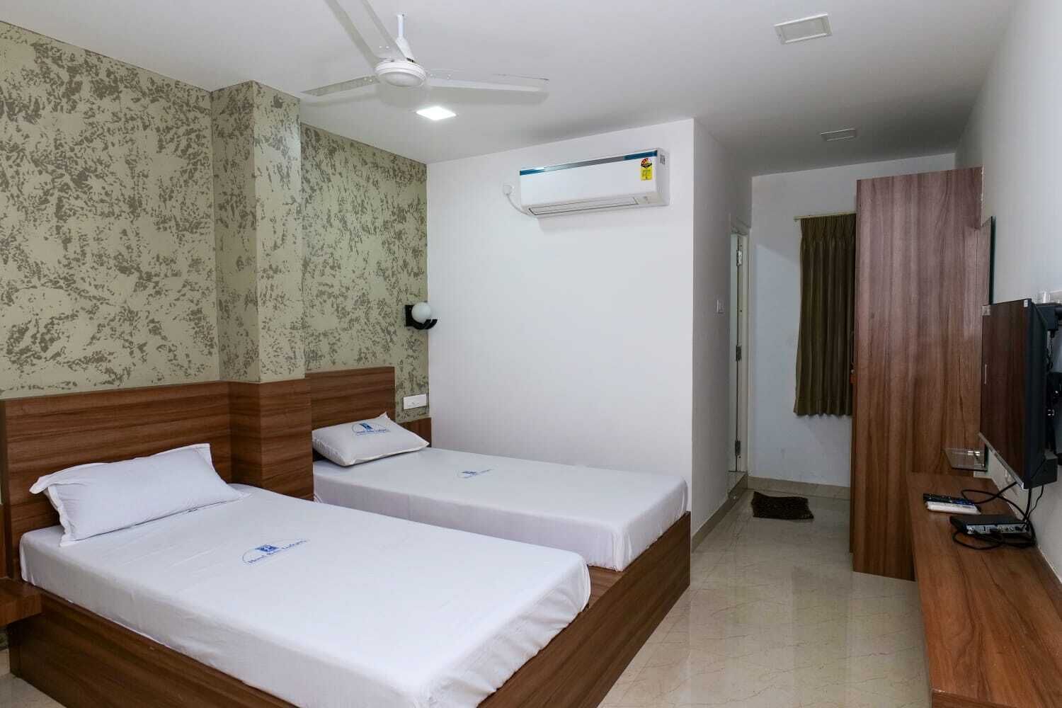 A hotel room with two single beds, a ceiling fan, an air conditioning unit, a television, and a wooden wardrobe.