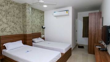 A hotel room with two single beds, a ceiling fan, an air conditioning unit, a television, and a wooden wardrobe.