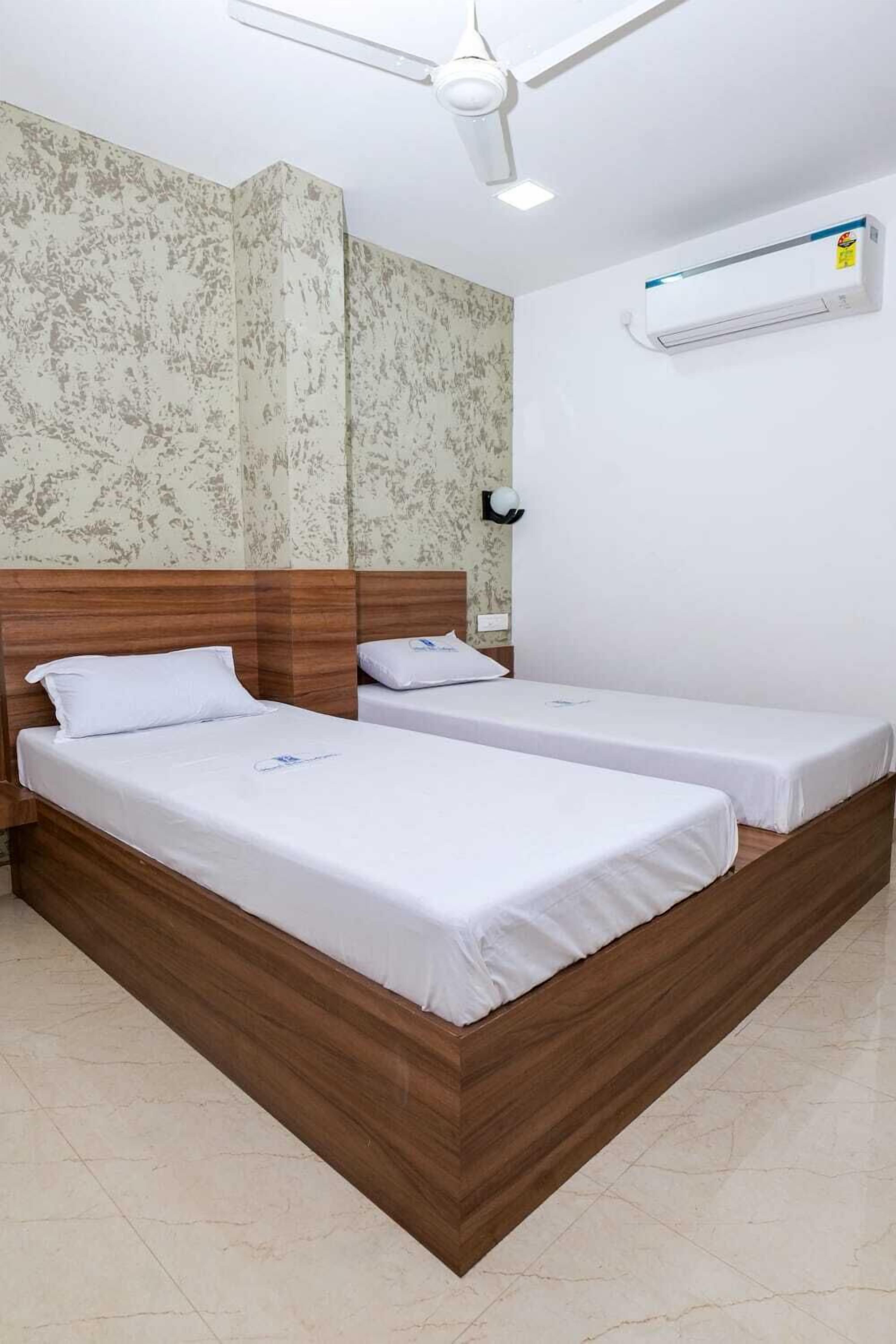A hotel room with two single beds, a ceiling fan, an air conditioning unit, and patterned wallpaper.