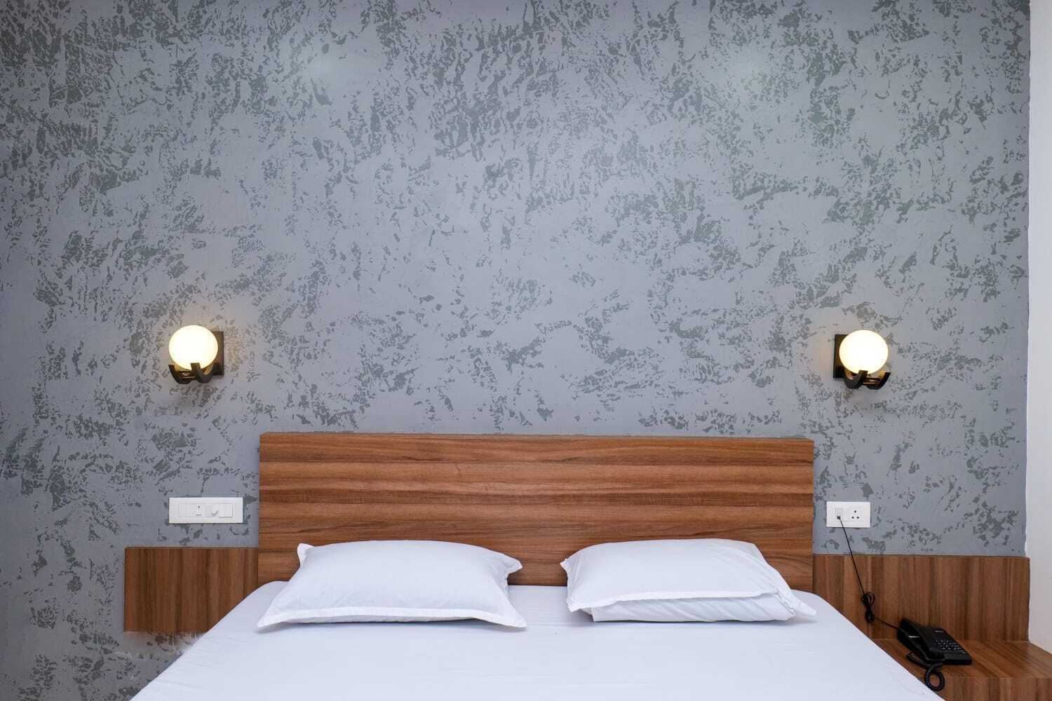 A hotel room with a wooden headboard, two white pillows, a white bedspread, and two wall-mounted light fixtures.