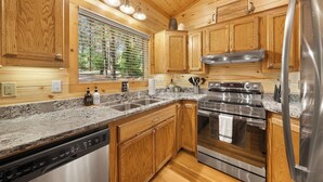 Una cocina con gabinetes de madera, encimeras de granito, electrodomésticos de acero inoxidable y una ventana con persianas.