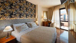 Ein Hotelzimmer mit Bett, Nachttischlampen, Schreibtisch, Stuhl und Blick ins Freie.